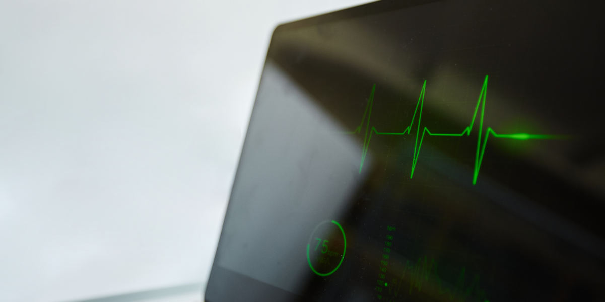 Close up of heart monitor display in hospital with child laying in bed in background, copy space