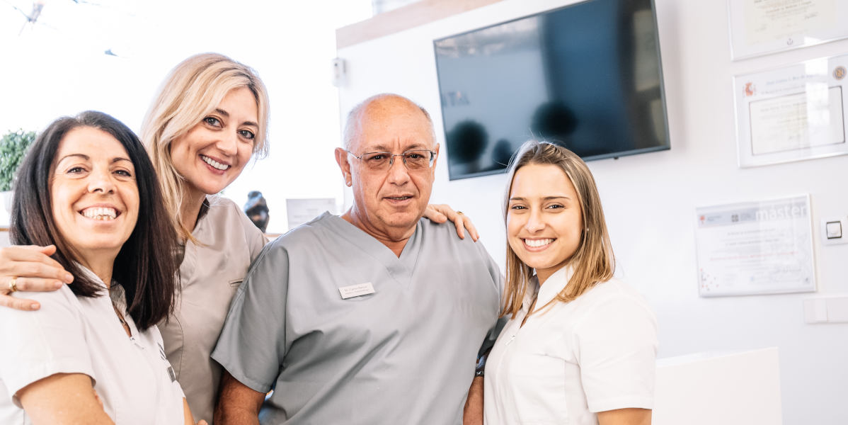 Positive young women and mature man in scrubs looking at camera and hugging each other while working in contemporary hospital together